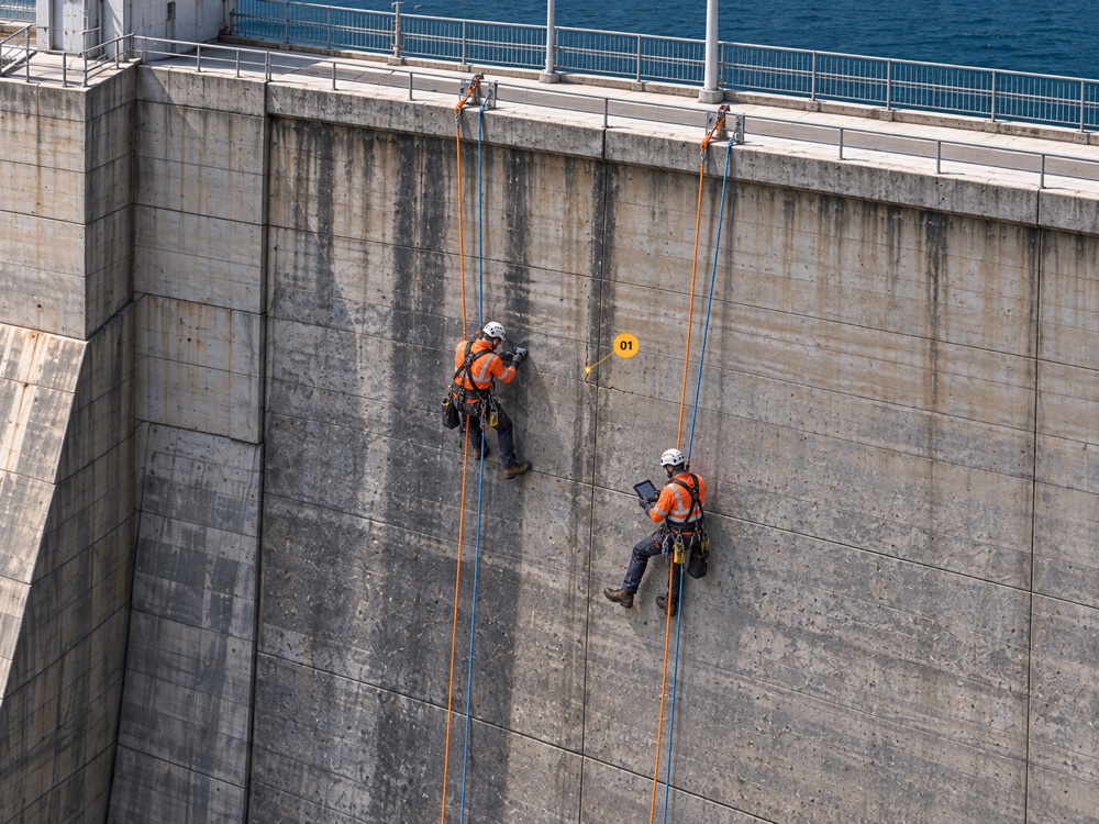 Two rope-access technicians working at a marked finding on the dam face